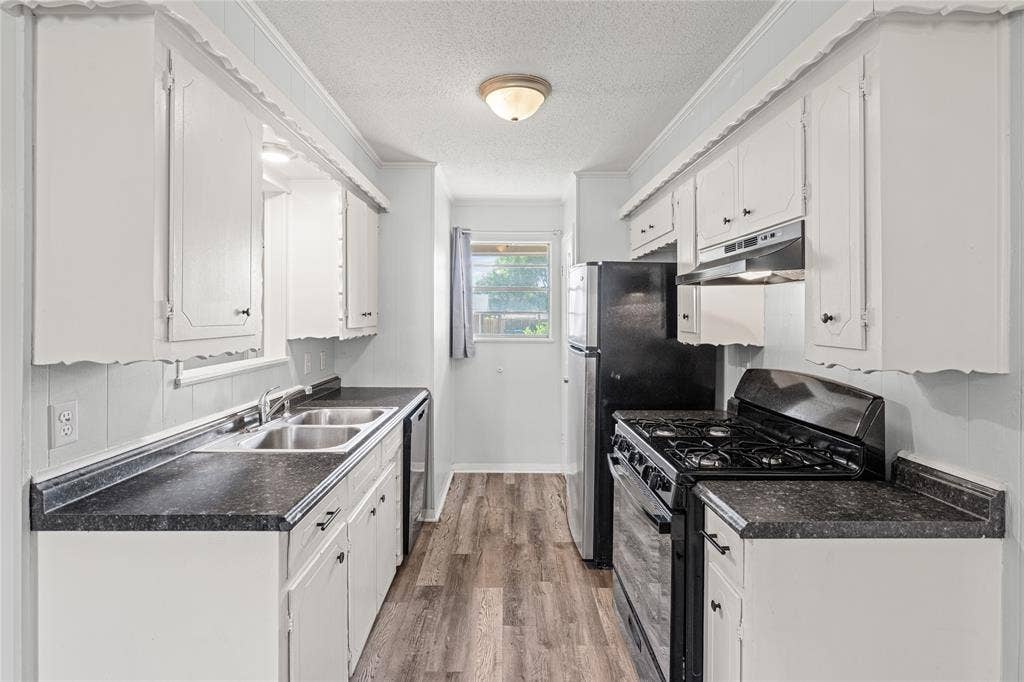 3407 Highmeadow Lane, Greenville, TX 75402 Galley kitchen featuring white cabinetry, dark countertops, wood-finish flooring, and a window for natural light