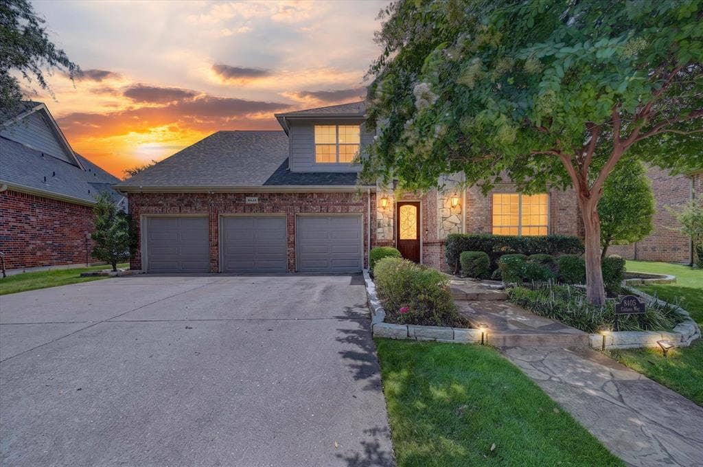 8405 Gallery Way, McKinney, TX 75072 Two-story residence featuring a combination brick and stone exterior, a concrete driveway leading to a three-car garage, and a covered entry with a decorative glass door