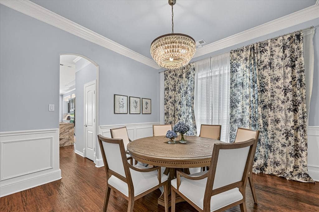 8405 Gallery Way, McKinney, TX 75072 Dining area featuring wood-finish flooring, wainscoting, an arched doorway, and a crystal chandelier
