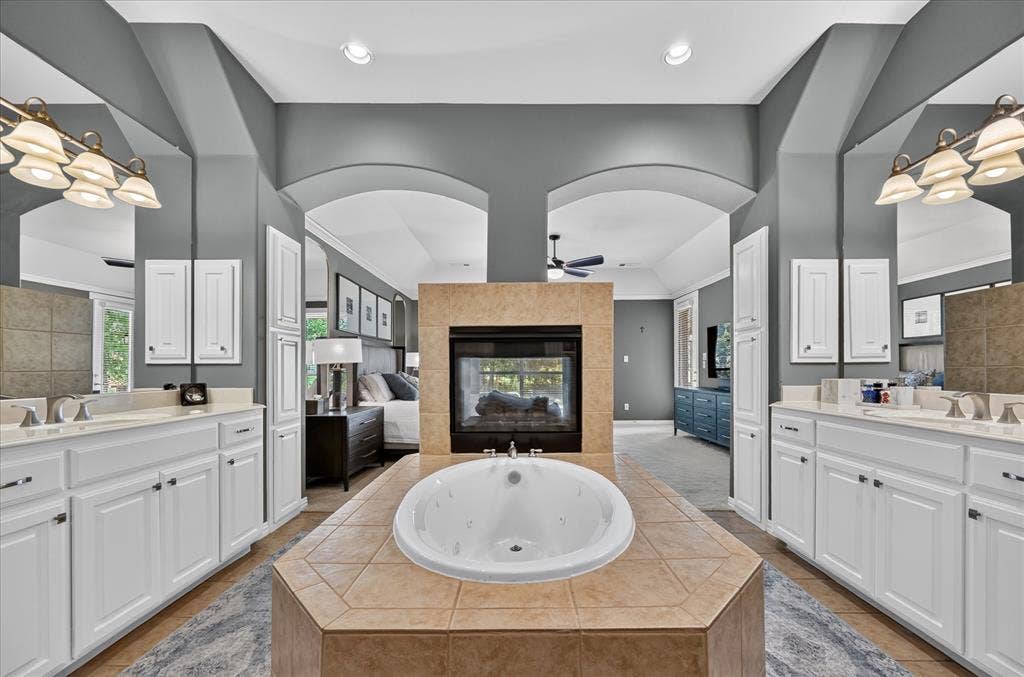 8405 Gallery Way, McKinney, TX 75072 Dual vanity sinks with white cabinetry, a built-in jetted tub, and a two-sided fireplace with tile surround