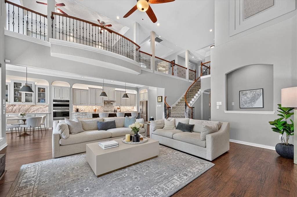 8405 Gallery Way, McKinney, TX 75072 Open concept living area featuring a two-story ceiling, wood-finish flooring, a gourmet kitchen with built-in appliances, a curved second-story balcony with wrought iron spindles, and a grand staircase