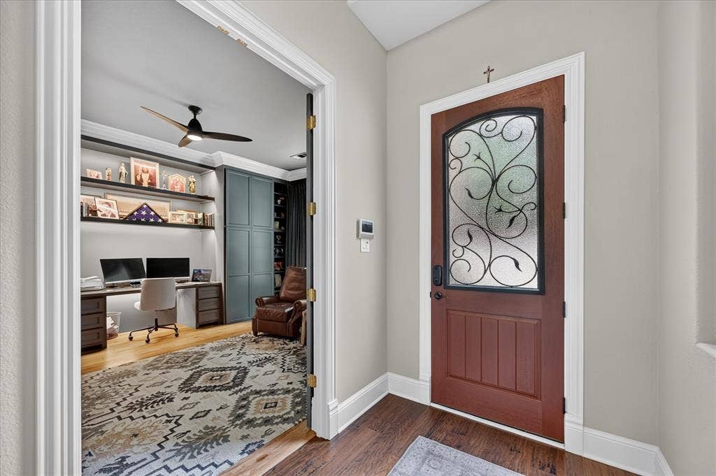 8405 Gallery Way, McKinney, TX 75072 Entryway featuring a wood door with decorative wrought iron and privacy glass, leading to a room with wood-finish flooring, built-in shelving, and a ceiling fan