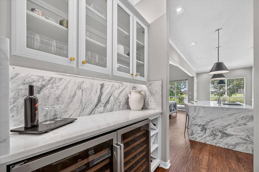 8405 Gallery Way, McKinney, TX 75072 Custom beverage station featuring a built-in wine refrigerator, white cabinetry with glass inserts, and a stone countertop with a matching backsplash