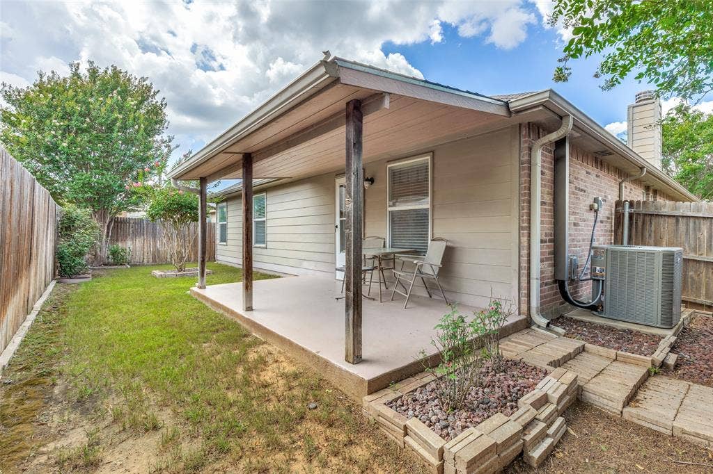 317 Amethyst Drive, Fort Worth, TX 76131 Covered concrete patio with wooden support columns, extending to a fenced backyard featuring a grassy area and mature trees
