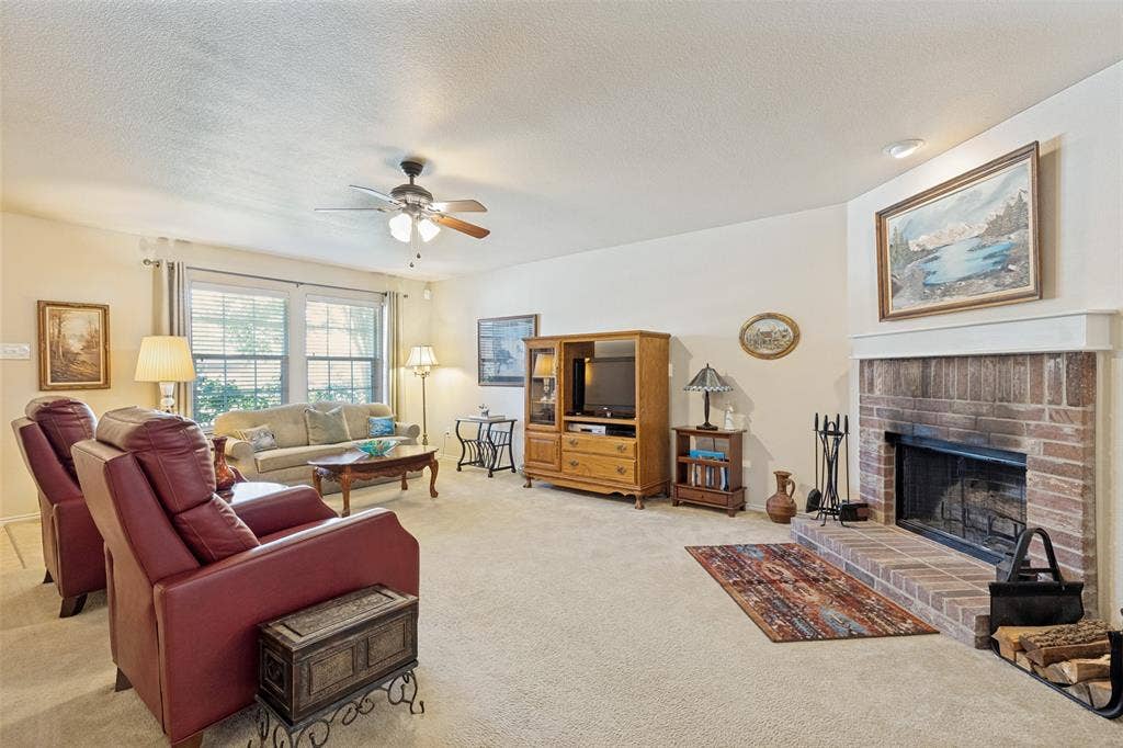 317 Amethyst Drive, Fort Worth, TX 76131 Living area featuring a brick fireplace with a painted mantel, neutral carpeting, a ceiling fan, and large windows with blinds
