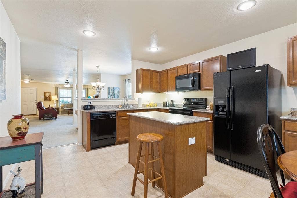 317 Amethyst Drive, Fort Worth, TX 76131 Kitchen featuring wood-finish cabinetry, black appliances, a central island with a light-toned countertop, and recessed lighting