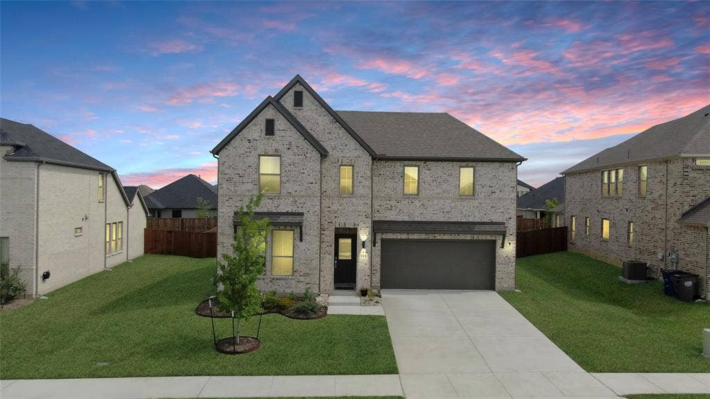 919 Edgehurst Drive, Princeton, TX 75071 Two-story brick exterior featuring a dark gray roof, an attached garage, a concrete driveway, and a manicured lawn with a young tree