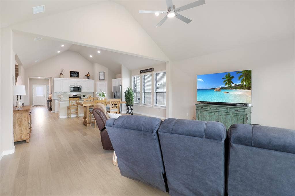 919 Edgehurst Drive, Princeton, TX 75071 Vaulted ceiling great room featuring light wood-finish flooring, recessed lighting, a ceiling fan, and a kitchen with white cabinetry and a built-in microwave