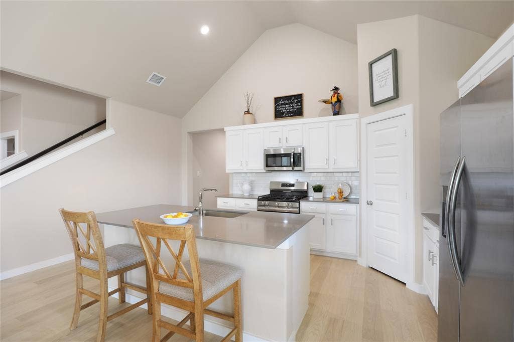 919 Edgehurst Drive, Princeton, TX 75071 Modern kitchen featuring a central island with integrated sink, stainless steel appliances, white cabinetry, and a subway tile backsplash