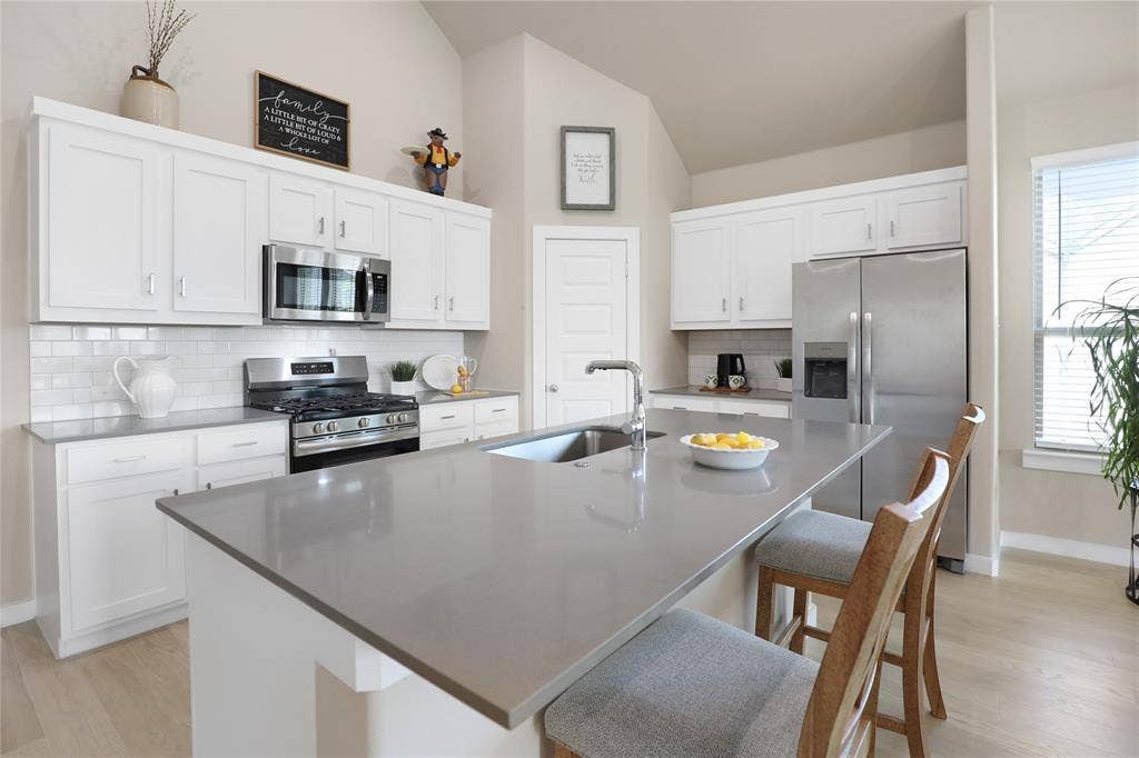 919 Edgehurst Drive, Princeton, TX 75071 Spacious kitchen featuring white cabinetry, stainless steel appliances, a light-toned subway tile backsplash, and a large island with a double basin sink and extended countertop seating