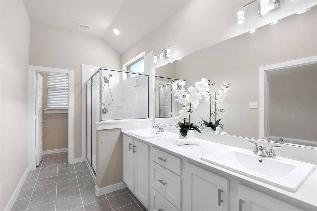 919 Edgehurst Drive, Princeton, TX 75071 Spacious bathroom featuring a dual vanity with white cabinetry and integrated sinks, a walk-in glass-enclosed shower, tile flooring, and a vaulted ceiling