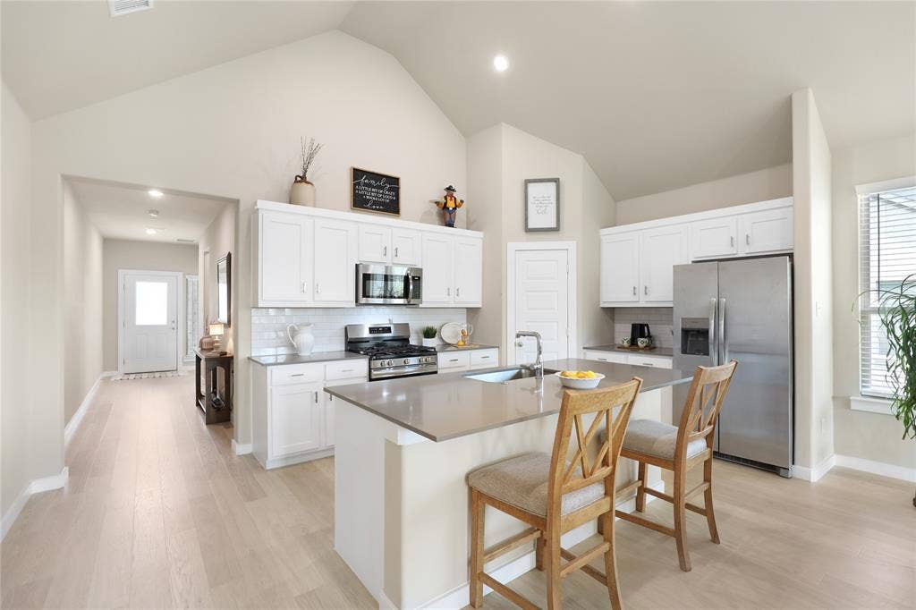 919 Edgehurst Drive, Princeton, TX 75071 Kitchen featuring a vaulted ceiling, white shaker cabinetry, stainless steel appliances, a center island with sink, and wood-finish flooring
