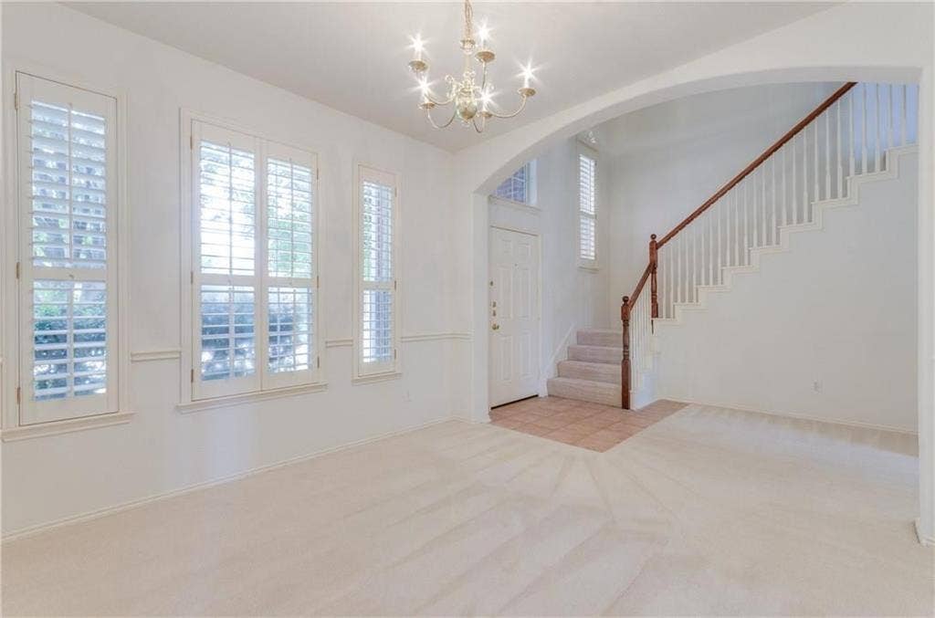 4440 Waskom Drive, Plano, TX 75024 Bright interior space featuring multiple windows with plantation shutters, a chandelier, a staircase with wood newel posts and handrail, and an arched entry