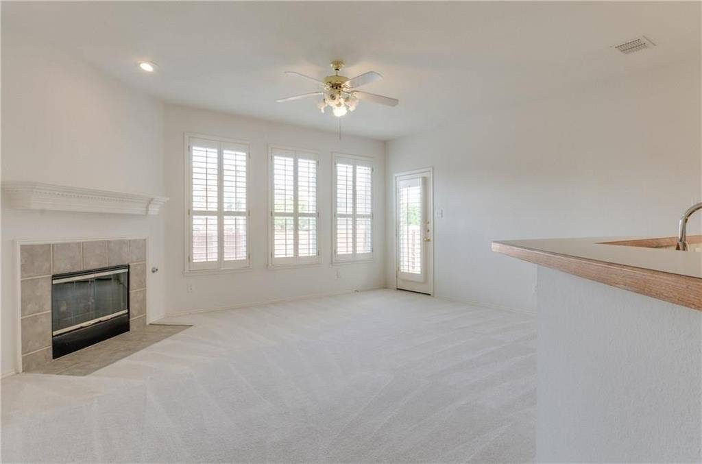 4440 Waskom Drive, Plano, TX 75024 Living area featuring a tiled fireplace with mantel, three windows with plantation shutters, a ceiling fan with integrated lighting, recessed lighting, and a door providing exterior access