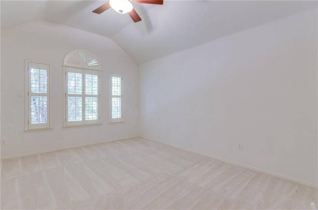 4440 Waskom Drive, Plano, TX 75024 Vaulted ceiling room featuring three windows with plantation shutters, arched transom window, ceiling fan with light fixture, and neutral carpet flooring