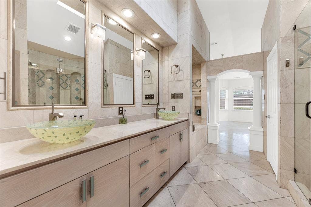 Symmetrical mirrors capture the classical white pillars framing the open passage to the bedroom. Experience a fluid, effortless transition as you step out of a warm bath directly into your sunlit dressing space.