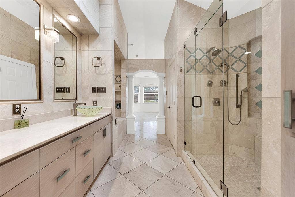 Seamless glass panels keep the sightlines open, blending the walk-in shower with the polished vanity area. Step onto the smooth, cool tiles wrapped in a plush robe to begin a slow, pampering weekend self-care ritual.