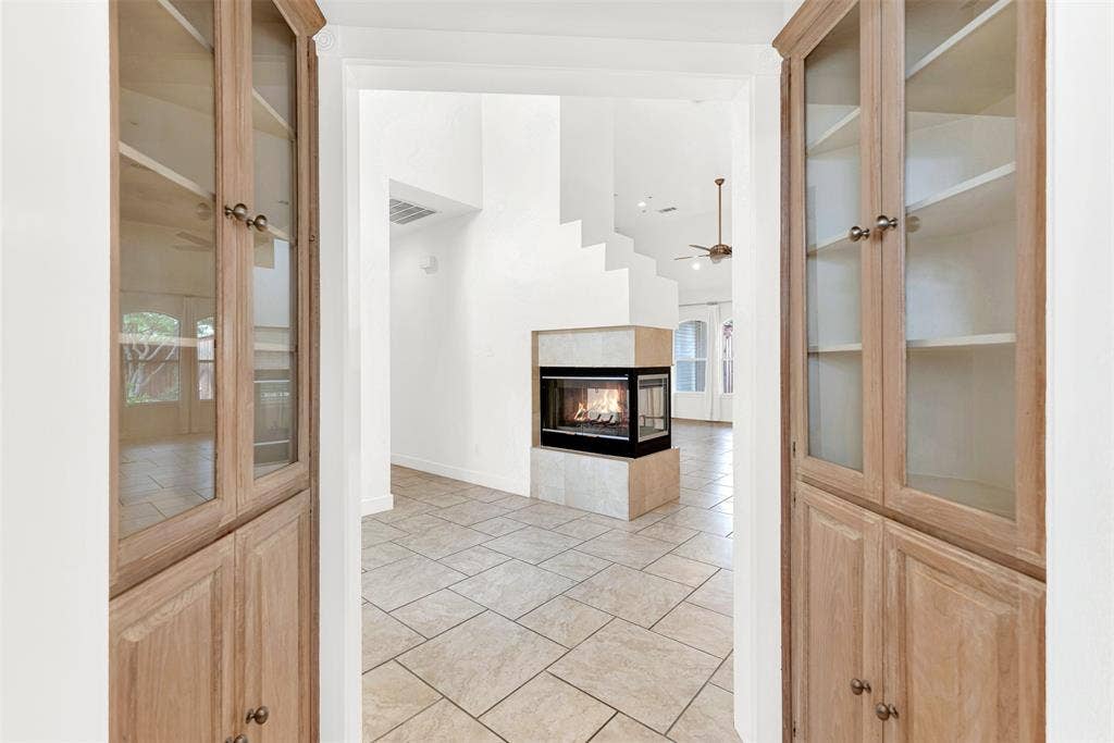 Custom glass-front built-in cabinets beautifully frame the sightline toward the open living spaces. Imagine pouring a morning coffee and glancing through to a glowing, warm hearth.