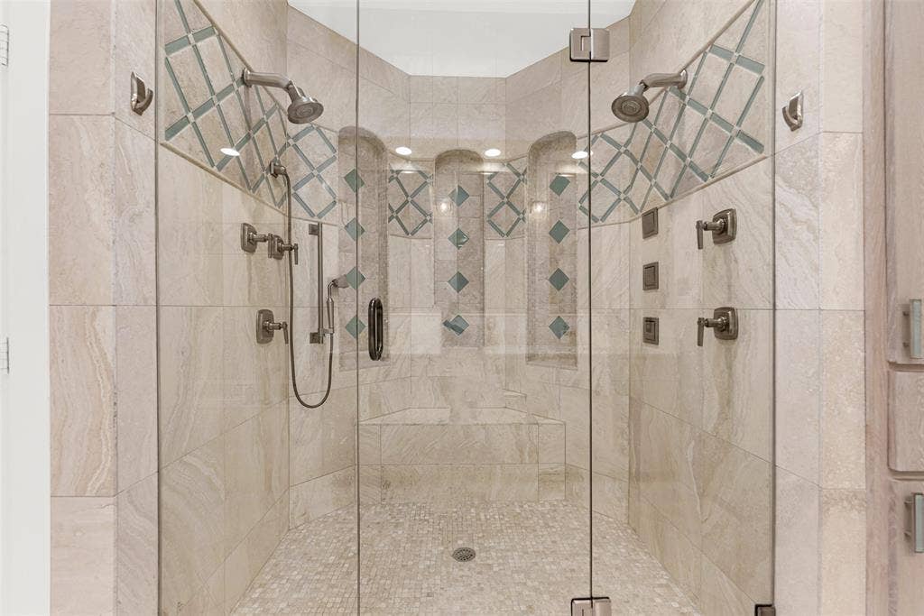 The glass-enclosed shower boasts dual heads, a built-in bench, and delicate mosaic-tiled niches. Indulge in a hot, steam-filled rinse that feels like a personal resort experience after a busy day.