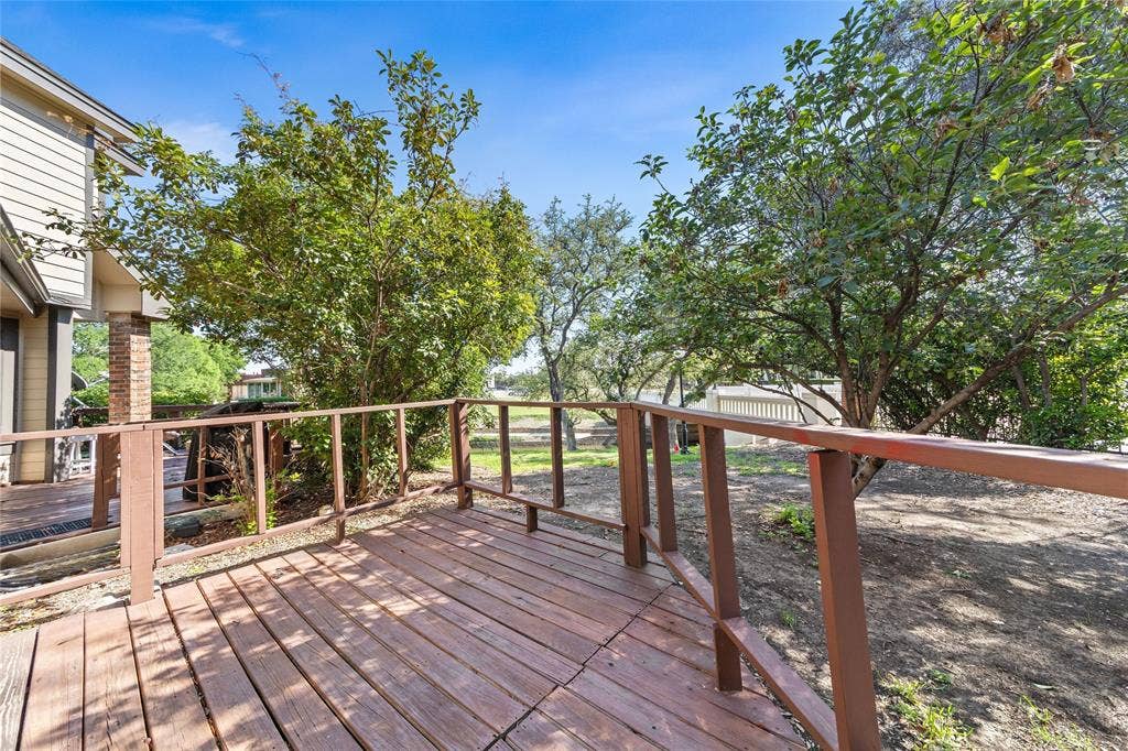 Exterior wood deck with railings, offering outdoor space surrounded by established trees and overlooking a creek with a spacious green buffer.
