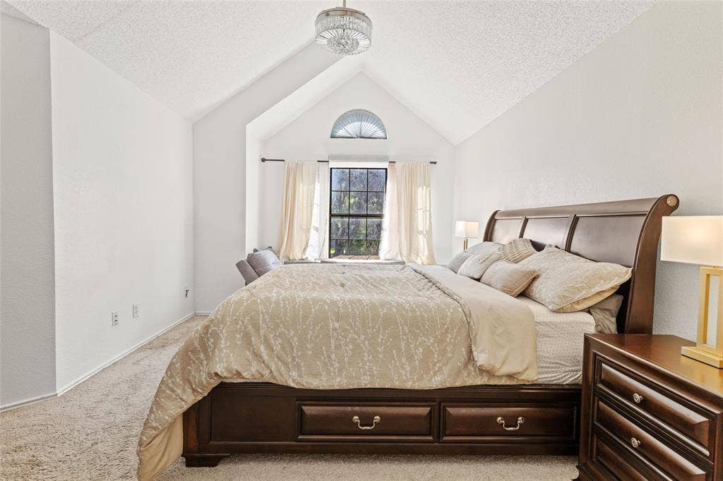 Vaulted ceiling bedroom featuring a semi-circular transom window, abundant natural light, and plush carpet flooring