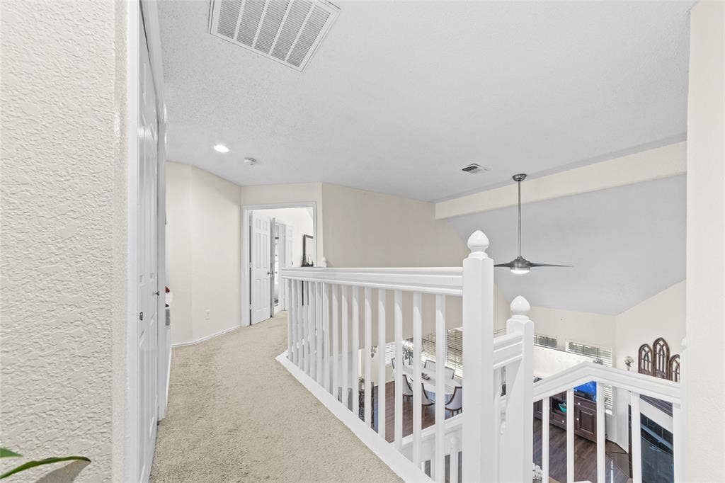Carpeted hallway overlooking a lower level, featuring white banister railings and a vaulted ceiling with a suspended light fixture