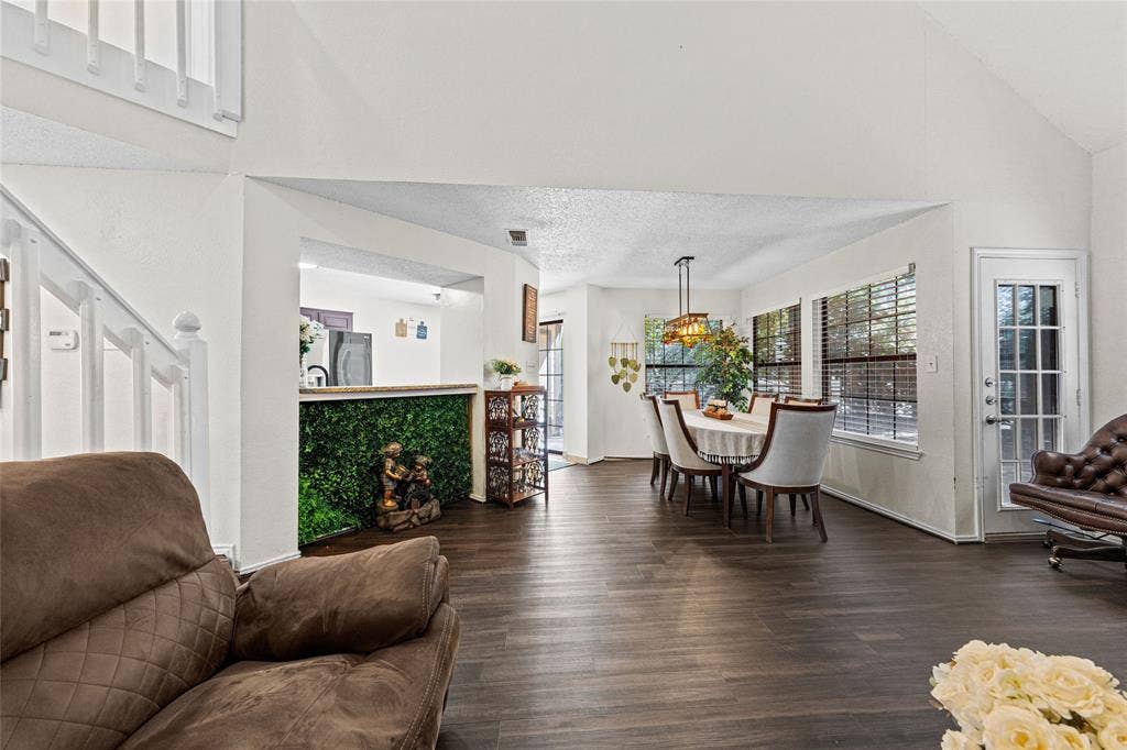 Open-concept living area featuring high vaulted ceilings, dark wood-finish flooring, and multiple large windows with blinds
