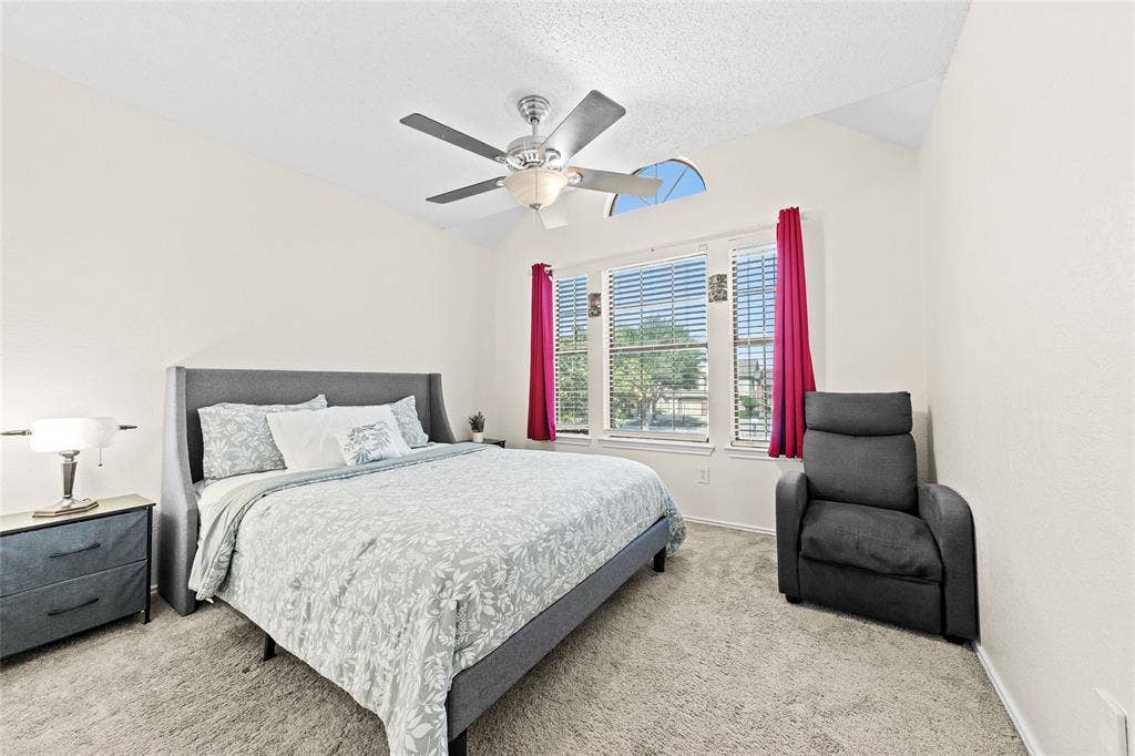 Carpeted bedroom featuring vaulted ceilings, a ceiling fan with integrated lighting, and multiple windows with blinds