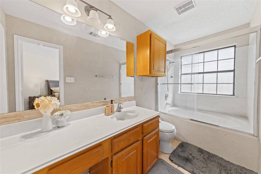 Bathroom featuring a vanity with a white countertop, wood-finish cabinetry, an integrated sink, and a large wall-mounted mirror