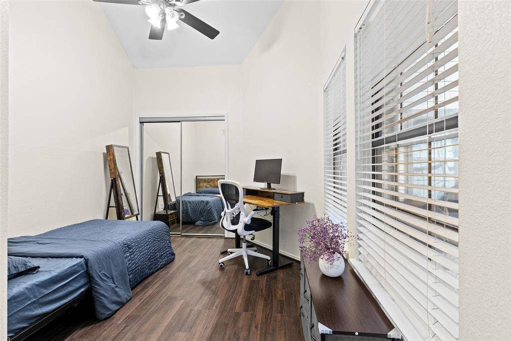 Vaulted ceilings enhance this room featuring dark wood-finish flooring, a ceiling fan, and mirrored closet doors