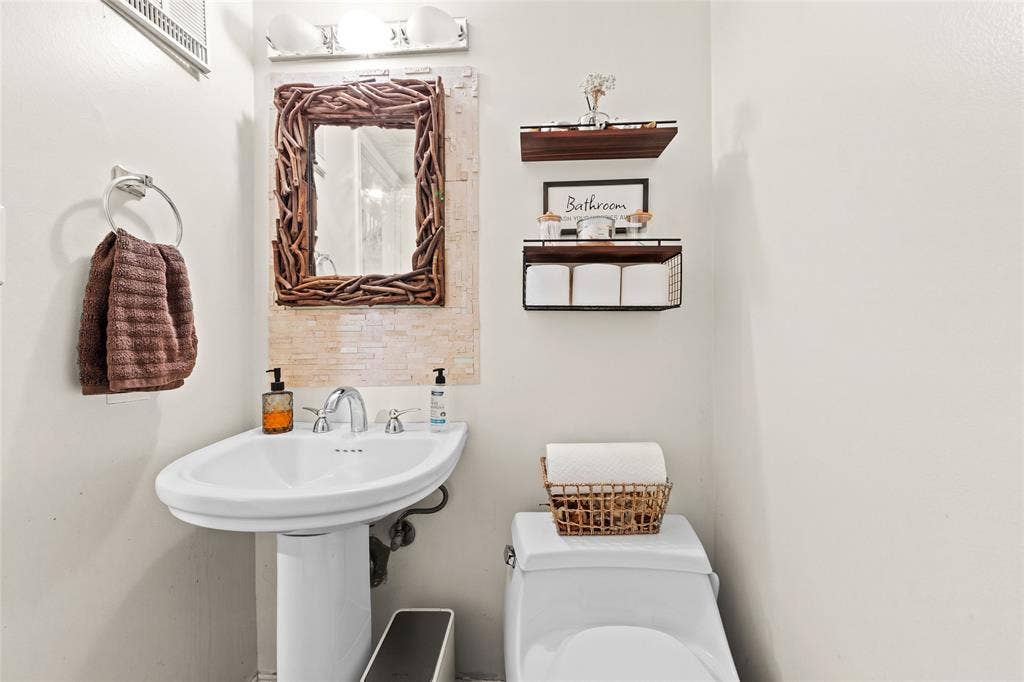 Pedestal sink with chrome faucet, complemented by a decorative mirror and vanity lighting
