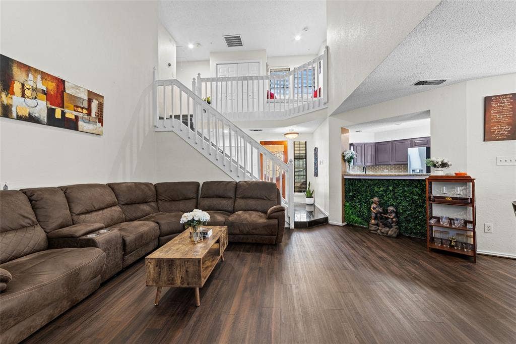 Spacious living area featuring wood-finish flooring, a prominent staircase with white railings, and an open concept layout with a kitchen pass-through