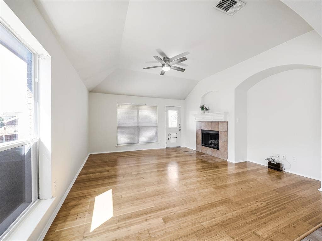 414 Dartmoor Drive, Celina, TX 75009 Vaulted ceiling living space featuring wood-finish flooring, a tiled fireplace with white mantle, and an arched wall opening