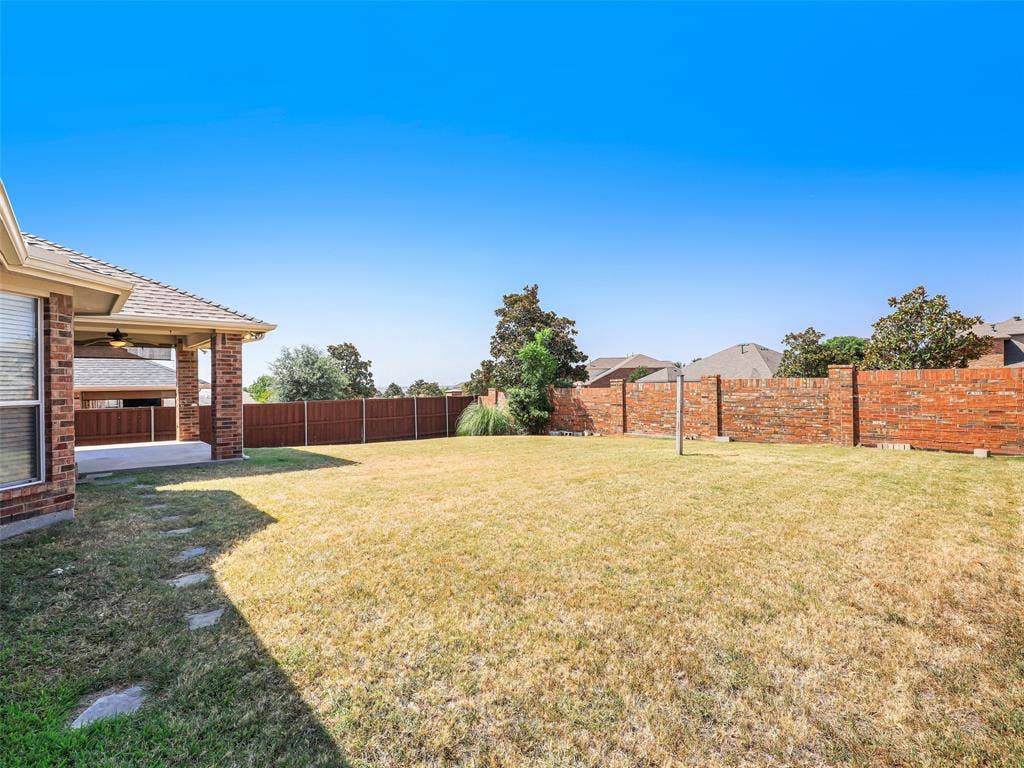 414 Dartmoor Drive, Celina, TX 75009 Angle showing the expansive green lawn space in the backyard of 414 Dartmoor Dr in Carter Ranch, Celina, Texas. Highlights include stepping stone pathways along the side, a combination of wood privacy fencing and a decorative red brick perimeter wall, and mature landscaping accents.