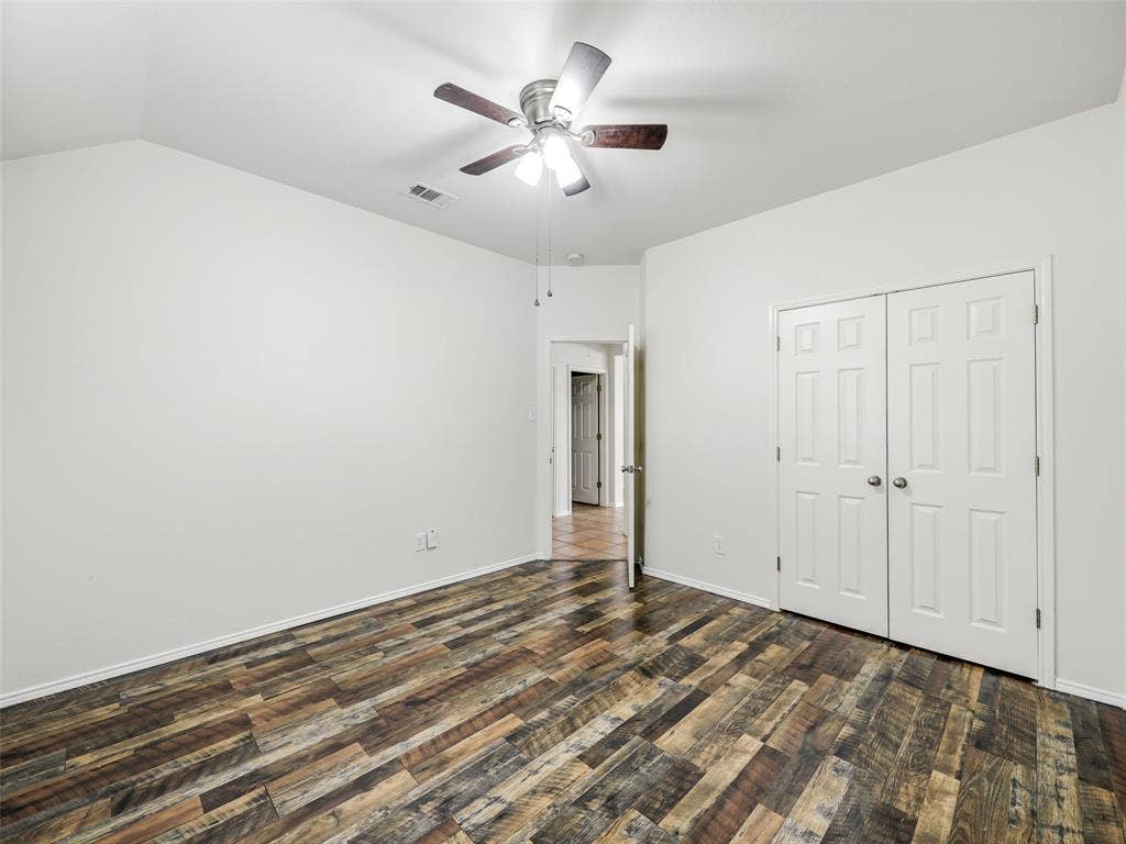 414 Dartmoor Drive, Celina, TX 75009 Reverse angle of the guest bedroom at 414 Dartmoor Dr, Celina, TX, showing the double-door closet and hallway entry. Highlights include cohesive multi-tone wood-look plank floors, crisp white trim and walls, and a ceiling fan with light fixture.