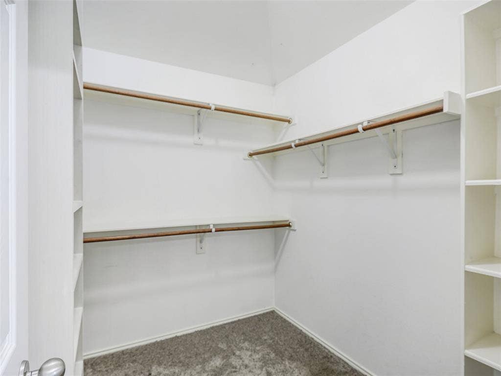 414 Dartmoor Drive, Celina, TX 75009 The walk-in primary closet at 414 Dartmoor Dr in Carter Ranch, Celina, TX. This organized closet system features neutral carpet flooring, built-in vertical shelving towers, and upper/lower multi-level hanging rods to maximize clothing storage space.