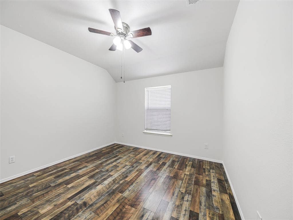 414 Dartmoor Drive, Celina, TX 75009 Reverse angle of the secondary bedroom at 414 Dartmoor Dr, Celina, Texas. Showcases the double-door closet, decorative chair rail trim, wood-look plank flooring, white ceiling fan, and direct doorway access to the adjacent guest hallway bathroom.