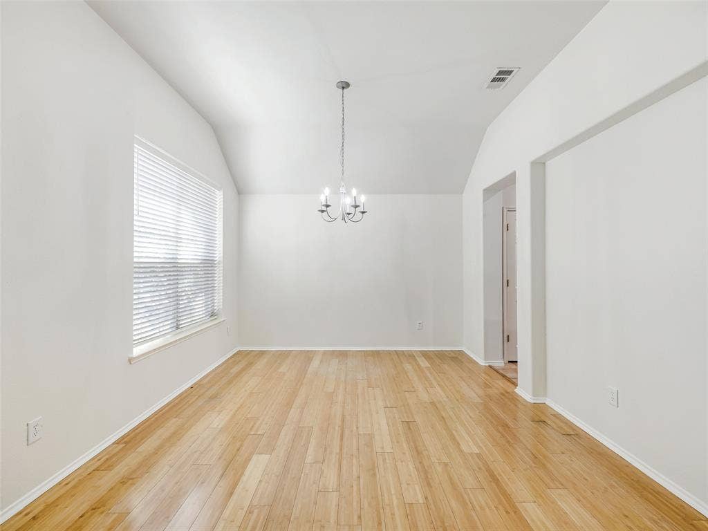 414 Dartmoor Drive, Celina, TX 75009 The formal dining room located immediately off the front entry foyer of 414 Dartmoor Dr, Celina, TX. This flexible space features durable light wood-look plank flooring, freshly painted white walls, a vaulted ceiling, and a large window with horizontal blinds for natural light. A decorative six-light candelabra chandelier hangs in the center of the room. This space can also serve as a dedicated home office.