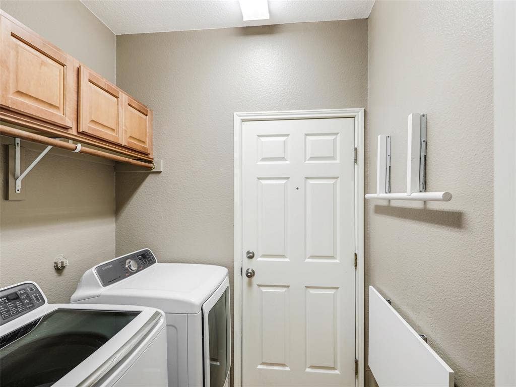 414 Dartmoor Drive, Celina, TX 75009 Dedicated interior laundry utility room at 414 Dartmoor Dr, Celina, Texas. Features washer and dryer hookups with Samsung appliances, built-in upper wood storage cabinetry, a clothing hanging rod, wall-mounted folding shelf racks, and direct interior access to the garage through a solid entry door.