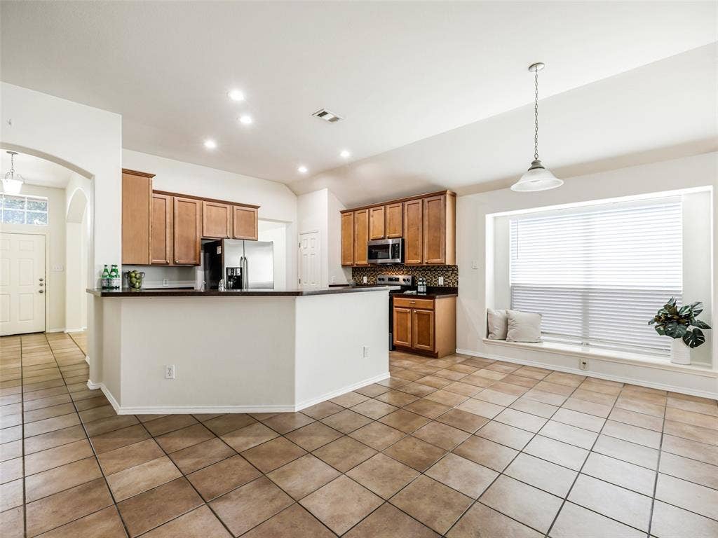 414 Dartmoor Drive, Celina, TX 75009 Wide shot showing the complete kitchen and eat-in breakfast nook area at 414 Dartmoor Dr in Celina, TX. The dining nook features ceramic tile flooring, a overhead pendant light, and a large bay-style window with a built-in window seat offering natural light and extra seating space.