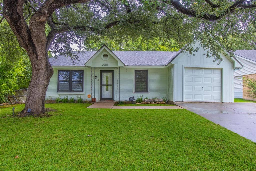 Single-story residence featuring light-colored siding, an attached garage, and a lush green lawn