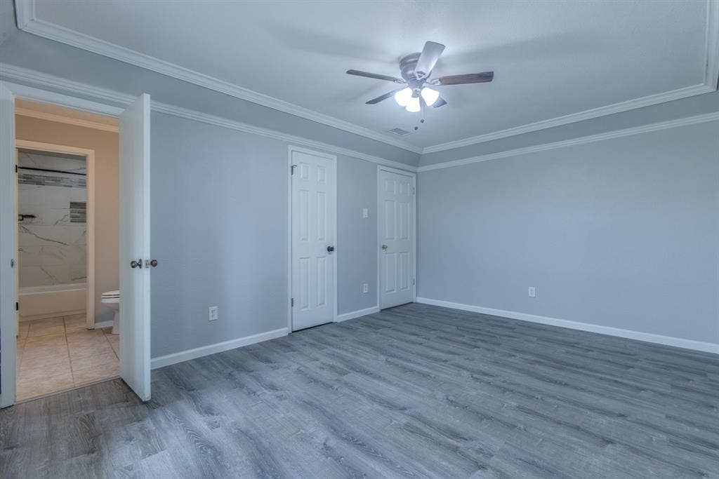 Spacious interior room featuring wood-finish flooring, light gray wall paint, and white crown molding