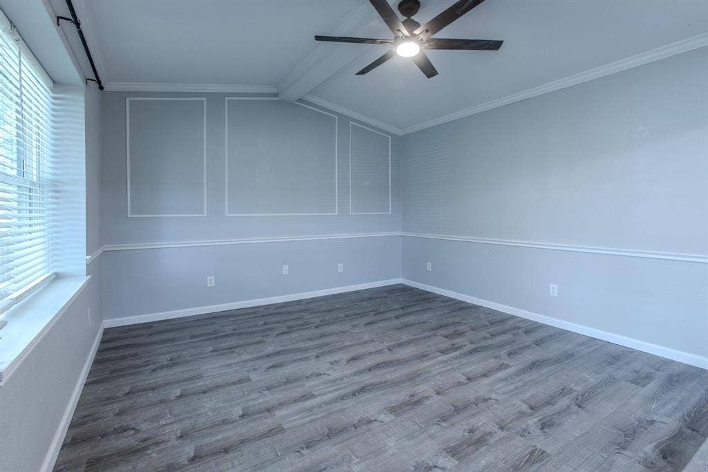 Spacious room featuring wood-finish flooring, a ceiling fan with integrated lighting, window blinds, decorative wall molding, and crown molding