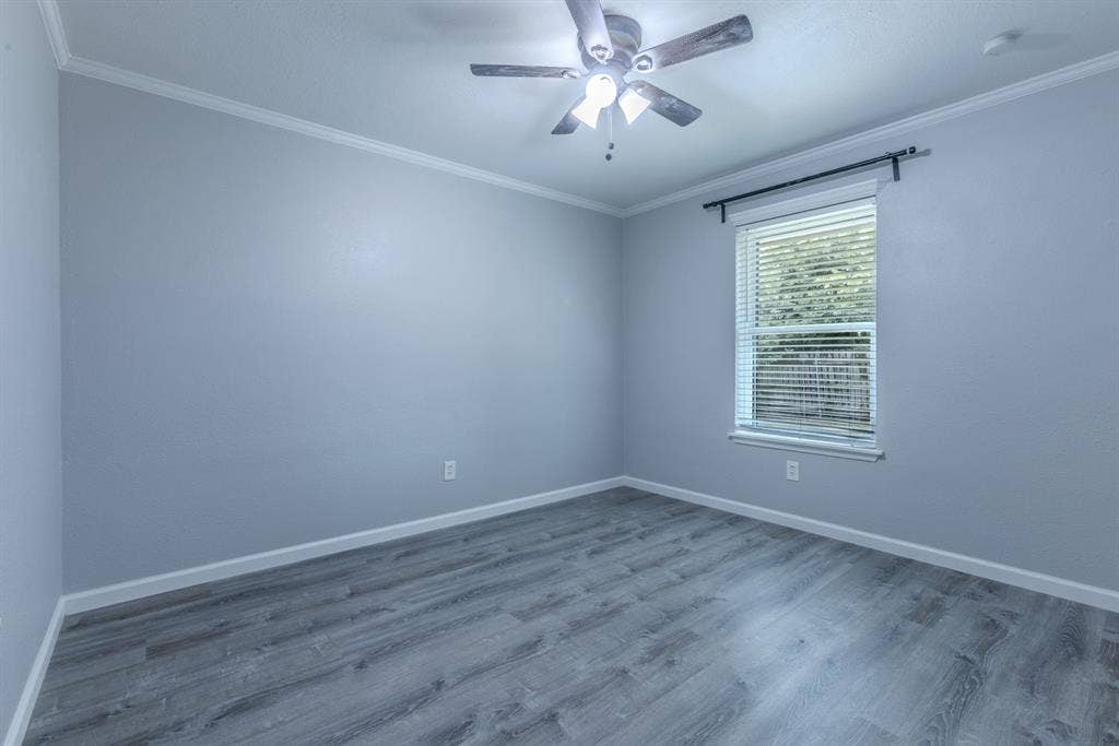 Room featuring wood-finish flooring, a ceiling fan with integrated lighting, and a single window with blinds and curtain rod