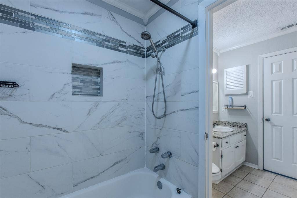 Bathtub shower combination featuring white marble-look tile, a decorative glass tile accent band, and a tiled shower niche