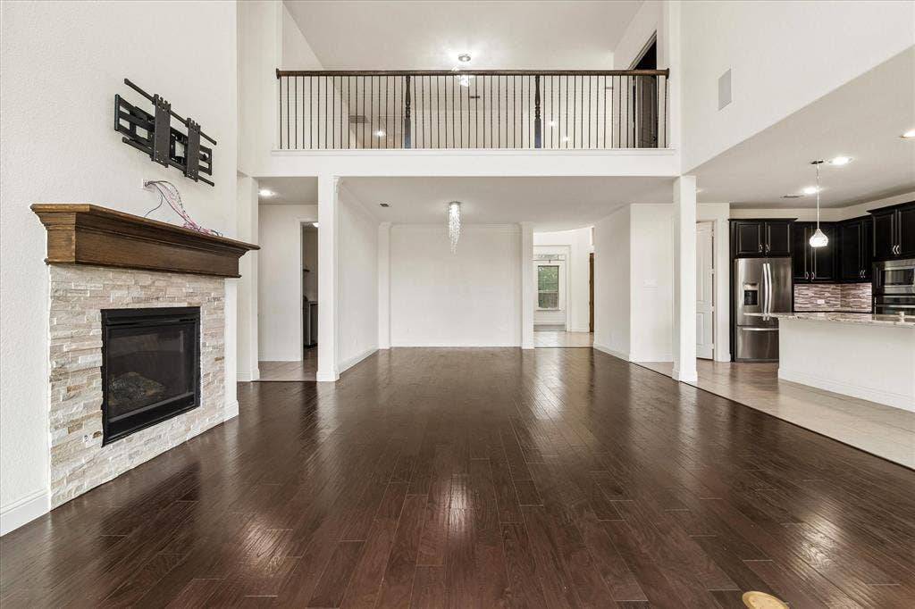 1650 Chisholm Trail, Prosper, TX 75078 Spacious living area featuring high ceilings, dark wood-finish flooring, and a stone-clad fireplace with a wood mantel