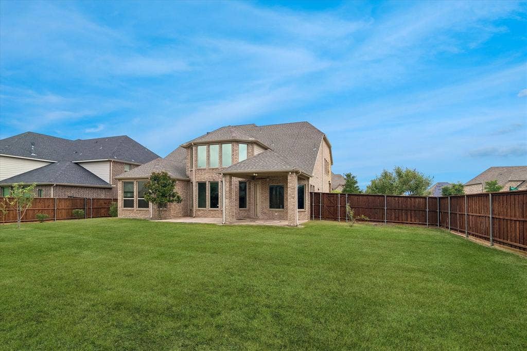 1650 Chisholm Trail, Prosper, TX 75078 Expansive backyard featuring a manicured lawn, a full privacy fence, a covered patio, and a two-story brick exterior with multiple large windows