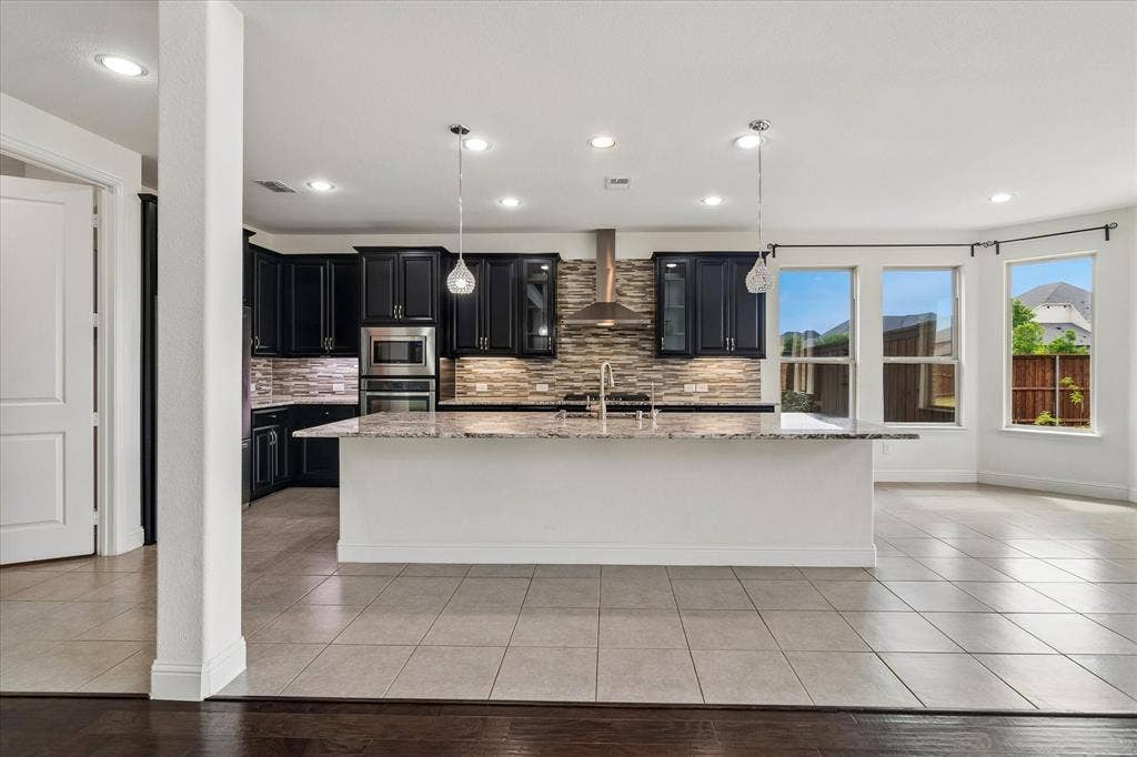 1650 Chisholm Trail, Prosper, TX 75078 Kitchen featuring an expansive island with a light-toned countertop, black cabinetry, stainless steel appliances, and a stacked stone backsplash
