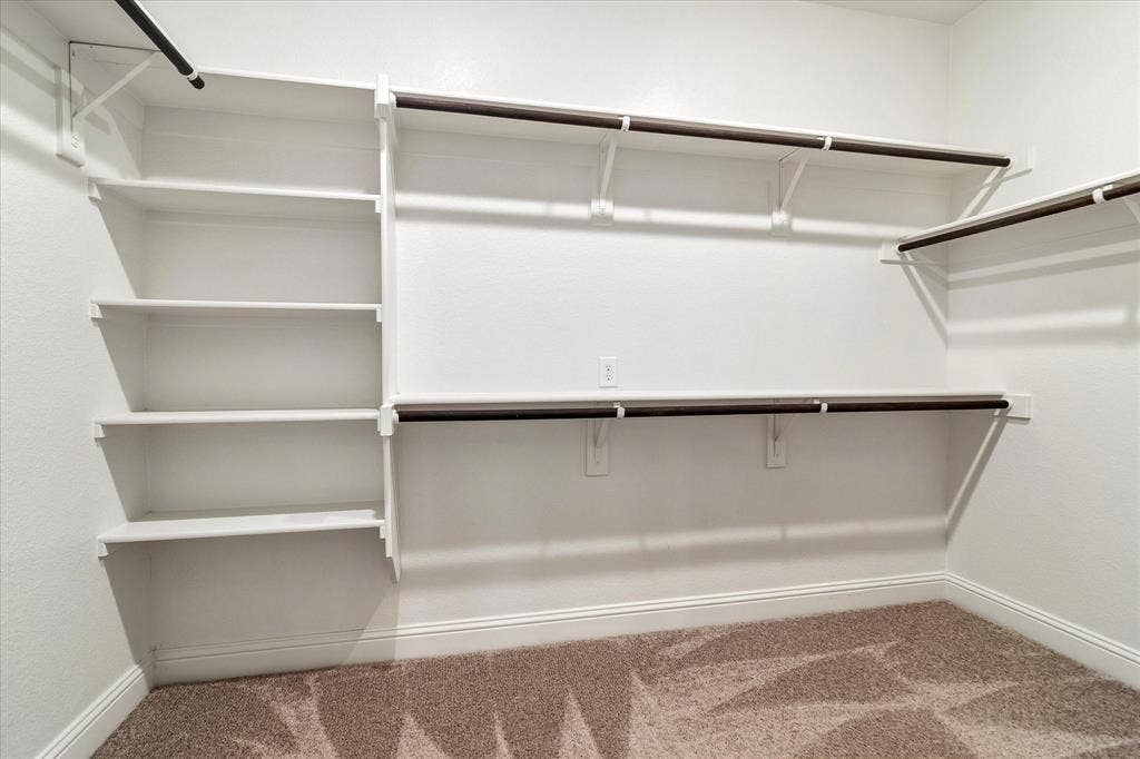 1650 Chisholm Trail, Prosper, TX 75078 Huge primary bedroom closet, Walk-in closet featuring built-in white shelving, multiple hanging rods, white walls, and neutral carpet flooring with baseboard trim