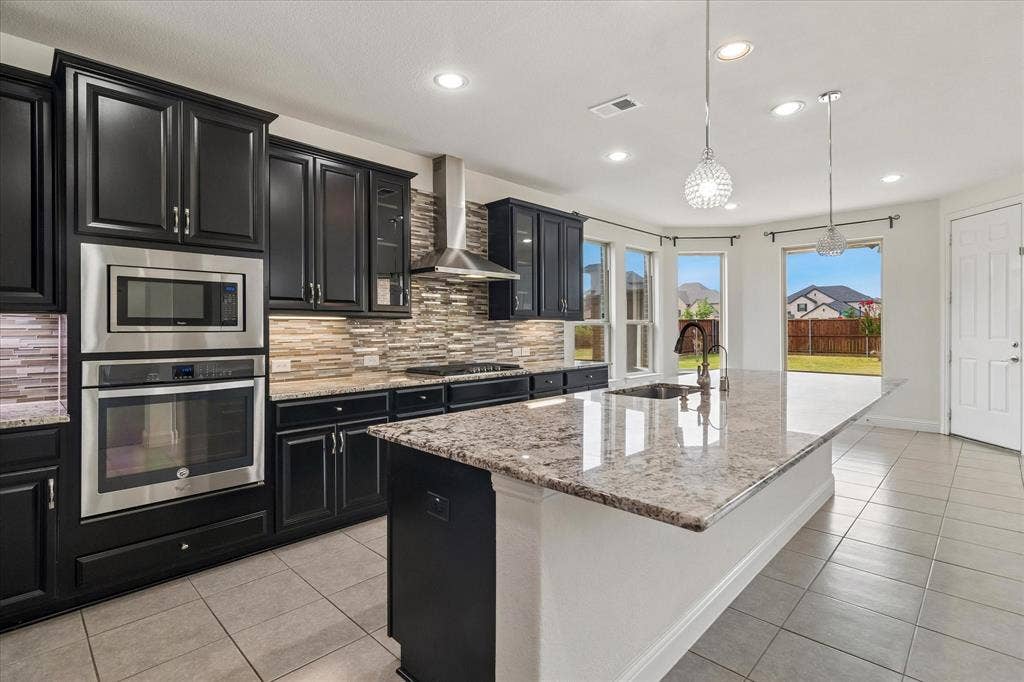 1650 Chisholm Trail, Prosper, TX 75078 Kitchen featuring dark wood cabinetry, stainless steel appliances, a tile backsplash, and a large center island with a light-toned countertop